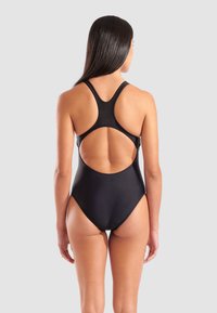Maillot de bain une pièce noir avec un design dos nageur, dos ouvert et texture lisse. Présente une silhouette ajustée et un matériel minimal.
