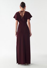 Bordová maxi šaty s V výstrihom a krátkymi rozšírenými rukávmi. Majú priliehavý siluet a bočný rázporok, vyrobené z hladkej látky.