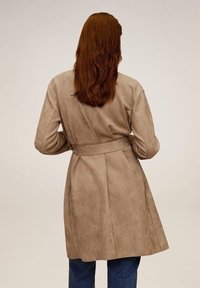 Beżowy, zamszowy trencz z paskiem w talii, długimi rękawami i swobodnym krojem, z plecami w klapki i gładką fakturą.