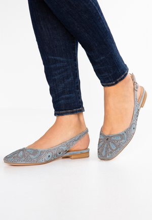Feet wearing gray slingback flats with blue decorative patterns and small studs, paired with dark blue skinny jeans.
