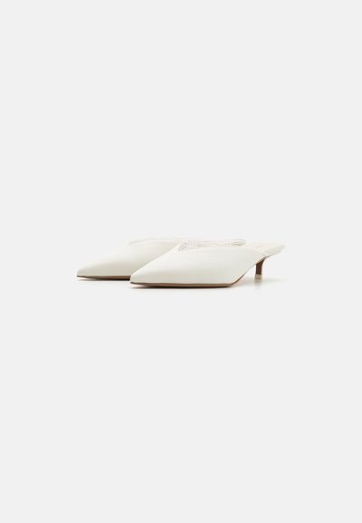 Mules blancos de satén sin talón con punta afilada, tacones bajos y adornos en la zona de los dedos. Textura suave con un diseño sencillo.