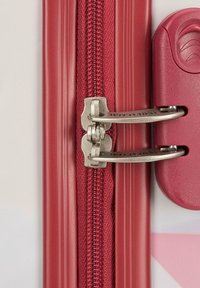 Zip de valise rouge avec deux tirettes métalliques, tissu texturé et un mécanisme de verrouillage en plastique ; accents de cadre lisses et durables.