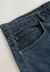 Tumedat sinised teksad sirge lõikega, peene whisker-mustriga ja väikese brändi etiketi ning tagumisel taskul.