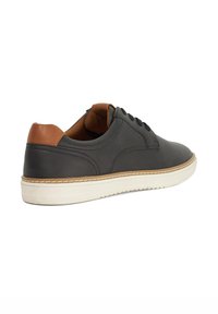 Black leather sneaker with brown leather heel accent, white rubber sole, and textured stitching detail. Laces for adjustable fit.