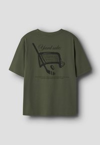 Oliven grøn t-shirt med sort grafik af en ishockeystav, puck og net samt tekst der står "Yard sale;" og en kort forklaring nedenunder.