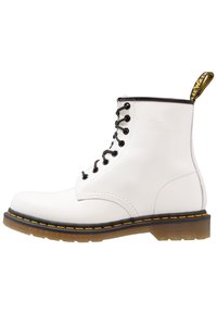 Botín de piel blanca hasta el tobillo con cordones negros, puntera redonda, costura amarilla y suela negra. Presenta un diseño resistente y ojetes reforzados.