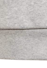 Tela de sudadera gris claro que muestra un tejido suave y texturizado con una costura visible en el dobladillo, presentando un sutil patrón de manchas.