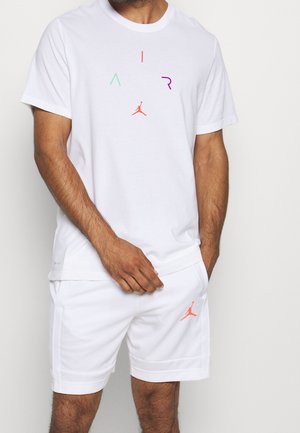 Mann in weißem kurzärmeligen Hemd und kurzer Hose, mit bunten AIR-Schriftzug und rotem Jumpman-Logo auf Hemd und Hose.
