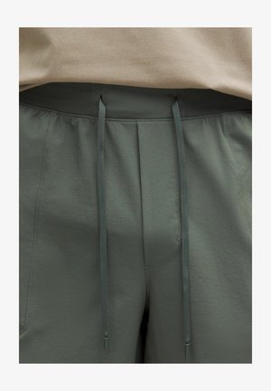 Primer plano de pantalones grises con cordón y tejido texturizado, junto a una camisa beige metida en la cintura.