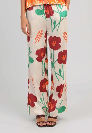 Pantalon crème à jambes larges avec un grand imprimé floral rouge et orange, porté avec des sandales marron à lanières et un haut orange à motifs.