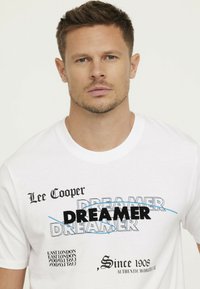 Weißes Baumwoll-T-Shirt mit "Lee Cooper" und "DREAMER" Grafiken in schwarzem, blauem und grauem Text. Standard Rundhalsausschnitt, kurze Ärmel und entspannter Schnitt.