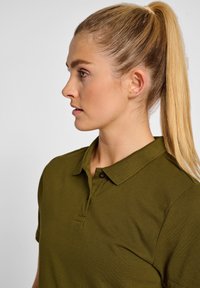 Oliwkowa koszulka polo o teksturowanej tkaninie, z zapięciem na dwa guziki i klasycznym kołnierzykiem; ma krótkie rękawy oraz dopasowany krój.