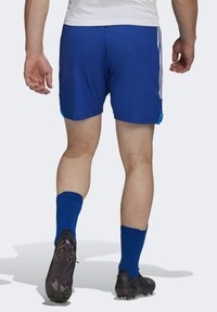 Blauwe sportshorts met witte zijstrepen, gedragen met blauwe sokken en zwarte voetbalschoenen. Zichtbare gespierde benen en gestroomlijnd ontwerp.