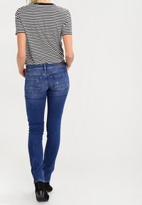 Tajta jeans i medelblå denim med en nära passform, fem fickor och lätta slitningar på baksidan. Kombineras med en randig skjorta.