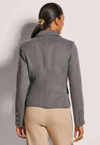 Grau Wollblazer mit tailliertem Design, Reverskragen und vierknöpfigen Akzenten an den Ärmeln. Glatte Stofftextur, maßgeschneiderte Silhouette.