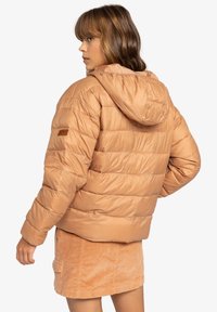 Blouson en beige clair avec des coutures horizontales, capuche ajustable et logo sur la manche, associé à une jupe en velours côtelé. Texture lisse.