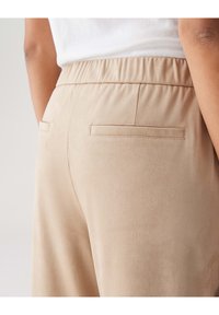 Pantalons beige clair avec une finition texturée semblable à du daim, dotés d'une taille élastique et de deux poches arrière avec des détails de couture discrets.