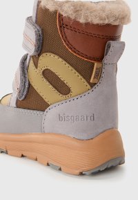 Gros plan sur une botte d'hiver pour enfants marron et grise avec des sangles en Velcro, doublure en polaire, semelle texturée et la marque "bisgaard" sur le talon.