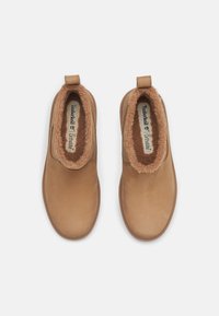 Bottines en suède marron avec une doublure en fausse fourrure douce, des tirants et des bouts ronds. Logo Timberland visible sur la semelle intérieure.