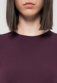 Bordo uska majica s kružnim izrezom, izrađena od glatkog materijala, s kratkim rukavima i elegantnim, minimalističkim dizajnom.