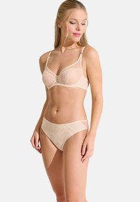 Soutien-gorge en dentelle beige avec des motifs floraux, bonnets avec armatures et bretelles réglables, assorti à une culotte de bikini au design similaire.