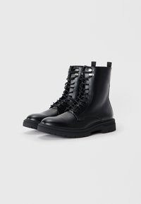 Botines de piel negra con cordones, punta redondeada, suela de goma gruesa y bucles en la parte trasera. Diseño minimalista sin patrones visibles.