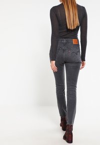 Mustat korkeavyötäröiset farkut, kapealla istuvuudella, valmistettu denimistä, jossa on nahkainen logopläsi takavyötäröllä ja hienovarainen haalistuma.