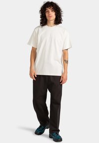 White cotton t-shirt with a classic crew neckline, paired with black wide-leg trousers and blue and black patterned sneakers.