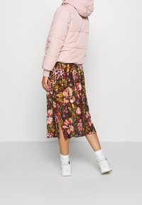 Světlá růžová péřová bunda s kapucí, doplněná květinovou sukní po kolena v odstínech červené, zelené a růžové a bílými teniskami.