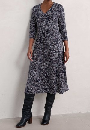 Granatowa sukienka w kwiatowy wzór, z dekoltem w serek i rękawami do połowy przedramienia; w zestawie z czarnymi skórzanymi kozakami do kolan na słupkowym obcasie.