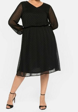 Czarna sukienka wykonana z przezroczystej tkaniny w kropki, z dekoltem w serek, długimi rękawami i dopasowaną talią, sięgająca tuż poniżej kolana.