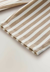 Pruun ja valge triibuline kangas tekstureeritud kudumisega, mille servadel on täpsed õmblused ja volditud äärepinda detail.