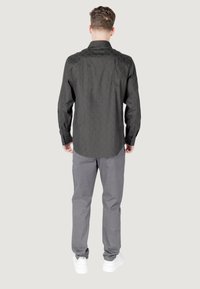 Maglietta nera a maniche lunghe con un motivo testurizzato sulle spalle, abbinata a pantaloni grigi a motivi e sneakers bianche.