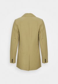 Blazer vert olive, design structuré, fente unique à l'arrière, revers à encoche, poignets boutonnés, tissu lisse avec une texture minimale.