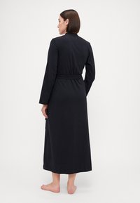 Robe noire en tissu doux, avec des manches longues, une taille ceinturée et un design long jusqu'au sol avec un ourlet droit.