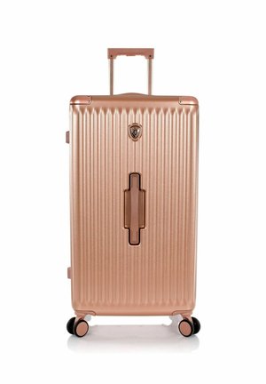 Grande valise rigide couleur or rose avec des rainures verticales, quatre roues, une poignée télescopique en haut et une poignée encastrée centrale.