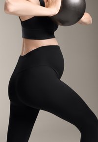 Fekete, magas derékú leggings, rugalmas anyagból, testhezálló fazon, sima textúrával. A modellen egy sötét kettlebell van, ami a profilját mutatja.