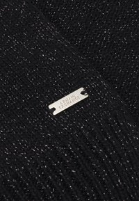 Tessuto knit nero con filo metallico, caratterizzato da un'etichetta logo argento che riporta la scritta "ARMANI EXCHANGE". Superficie testurizzata con un delicato luccichio.