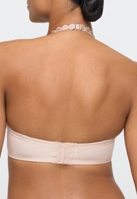 Der Rücken einer Frau, die einen trägerlosen Nude-BH mit Drei-Haken-Verschluss und eine dekorative Spitzenhalskette trägt.