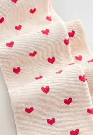 Knee-high socks in light pink with red heart patterns. The fabric features a ribbed texture, highlighting the repeating heart design.