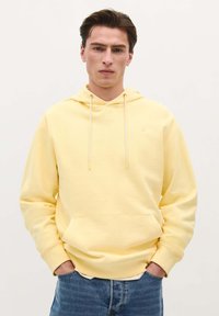 Geel hoodie met een voorzak in kangoeroestijl, met koordjes en geribbelde manchetten, gecombineerd met blauwe denim jeans. Soepele stoftextuur.
