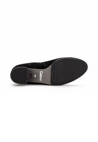 Black suede low-heeled shoe with a textured sole and a smooth, curved back. Features a subtle brand logo on the insole.