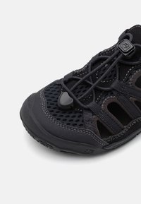 Melnas sieta āra kurpes ar gumijas zoli, elastīgu pēdu sasaistes sistēmu un sānu izgriezumiem ventilācijai. Tekstūras akcenti uzlabo saķeri.