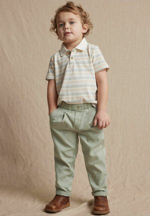 Polo à manches courtes rayé dans des tons beige et blanc, associé à un pantalon à taille élastique vert clair et des bottines marron avec des détails texturés.