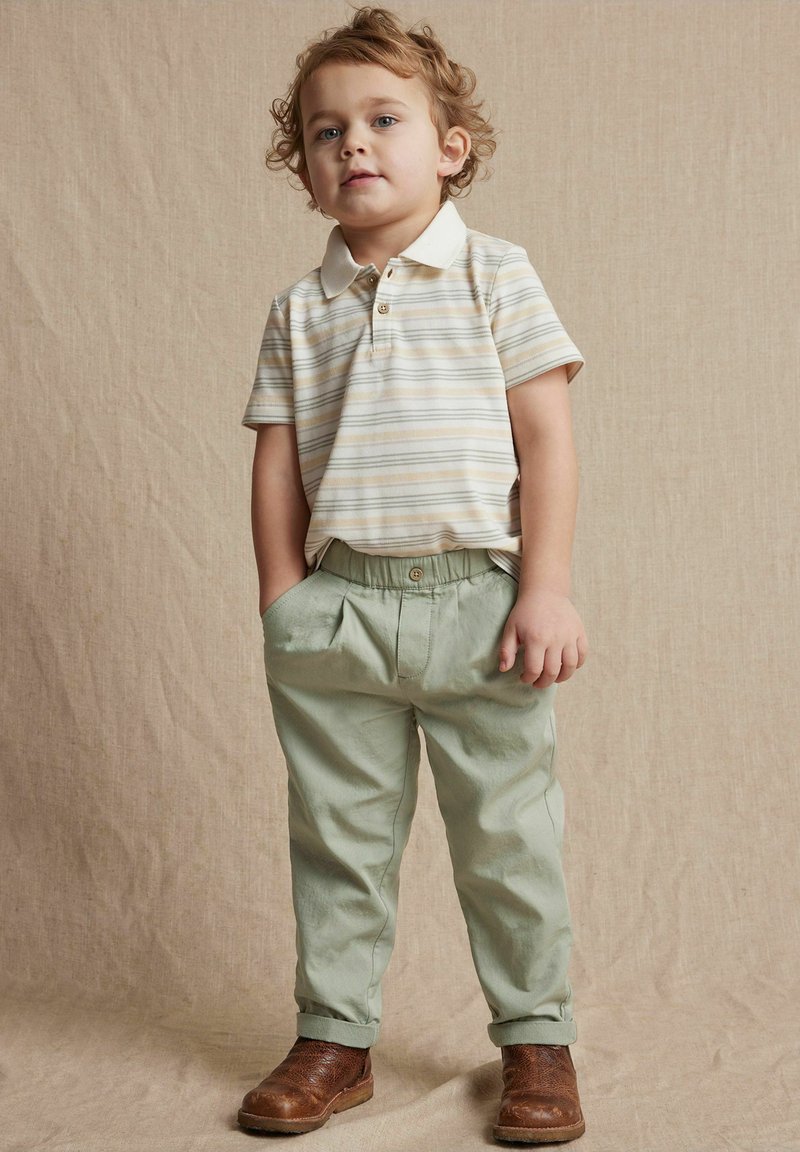 Polo à manches courtes rayé dans des tons beige et blanc, associé à un pantalon à taille élastique vert clair et des bottines marron avec des détails texturés.