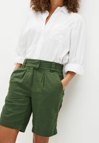 Weißes Hemd mit umgeschlagenen Ärmeln und grünen Leinen-Shorts mit einem gefältelten Design und elastischem Bund.