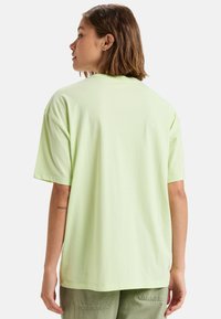 Camiseta de manga corta de color verde claro con un ajuste relajado, hecha de material de algodón suave. Presenta un dobladillo recto y un diseño sencillo sin adornos.
