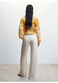 Gelb gemusterte Bluse mit Puffärmeln, kombiniert mit cremefarbenenweiten Hosen. Sanfte Textur und lockere Passform. Gemalter Hintergrund.