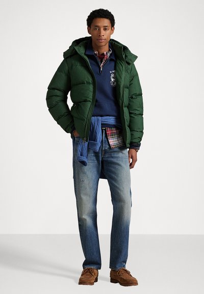 Grön puffjacka med huva, blå sweatshirt, rutig skjorta, denimjeans och bruna skor; lager av texturer och varierade färger.