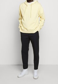 Sweat à capuche en coton jaune avec cordons de serrage, associé à un pantalon noir slim et des baskets blanches montantes. Design simple et coupe décontractée.
